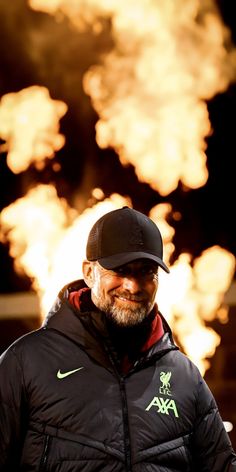 a man wearing a black hat and jacket standing in front of a firework display