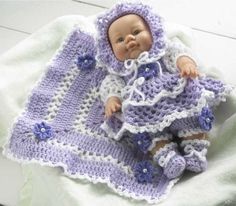 a crocheted baby doll laying on top of a blanket with purple and white flowers