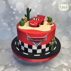 a red cake with cars on it and cactuses around the edges, sitting on top of a black plate