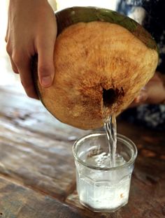 a person pouring water into a glass on top of a wooden table next to a banana