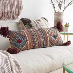 a white couch with two pillows on top of it and some plants in the corner