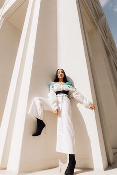 a woman leaning against the side of a tall white building with her legs spread out