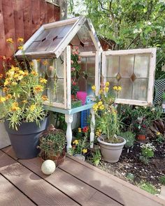 an outdoor garden with potted plants, flowers and a small house shaped like a greenhouse