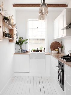 an all white kitchen with wood floors and hanging lights over the sink, along with open shelving