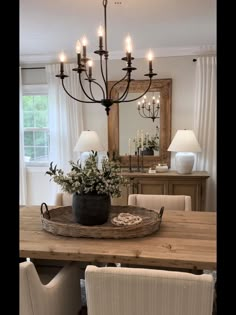 a chandelier hanging over a wooden table in a dining room with white chairs