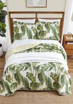 a bed with green leaves on it in a room next to a potted plant