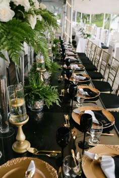 a long table is set with black and gold plates, silverware, and greenery