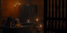 a woman sitting in a bathtub with candles on the floor next to her,