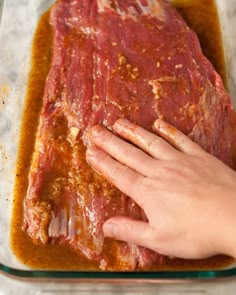 a person touching the meat on top of a pan filled with sauce and seasoning