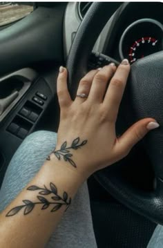 a woman's hand on the steering wheel of a car with an olive branch tattoo