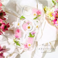 an iphone case with flowers on it sitting next to some white cloth and pink flowers