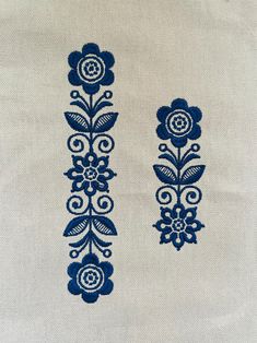 two blue flowers on white fabric with dark blue trimmings, one in the shape of an arrow