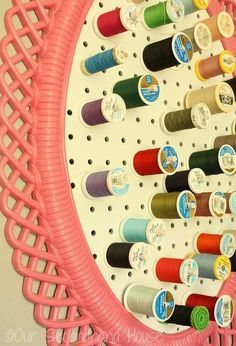 there are many spools of thread hanging on the wall behind this pink rack