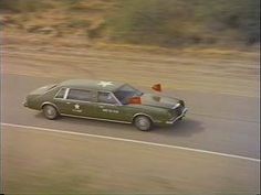 an old green car driving down the road