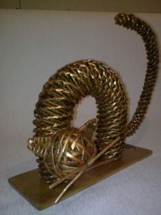 a gold sculpture is sitting on top of a white surface and has two balls of yarn wrapped around it