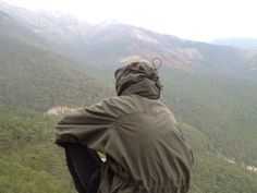 a man sitting on top of a mountain looking down at the valley below his jacket