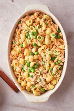 a bowl filled with pasta and peas next to a wooden spoon on top of a table