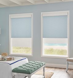 a bedroom with blue walls and two windows that have roman shades on them, along with a bench in front of the window