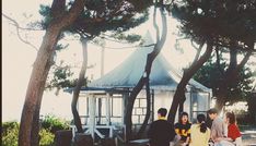 several people standing around in front of a gazebo with trees and rocks on the ground