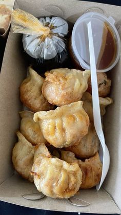 an open box filled with pastries next to a bowl of sauce and a spoon