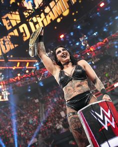 a woman with tattoos holding up a wrestling belt