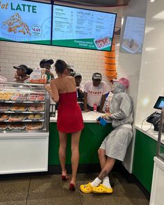 a woman in a red dress is ordering food at a deli counter with other people