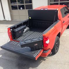 an orange truck with its bed open in front of a garage door and two black boxes on the back