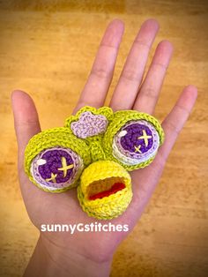 a hand holding a small crocheted toy with two eyes and a smiley face