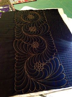 a black piece of fabric with an intricate design on the front and side, sitting on top of a cutting board