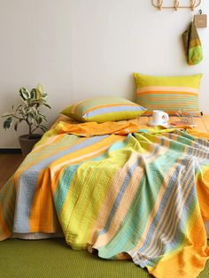 a bed with colorful blankets and pillows on it in a room next to a potted plant