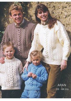 an adult and two children wearing sweaters standing next to each other in front of a stone wall