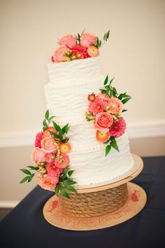 a three tiered white cake with pink flowers on top and green leaves around the edges