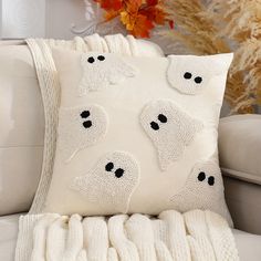 a white pillow with black eyes on it sitting on a couch next to a plant