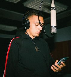 a man wearing headphones is looking at his cell phone in front of a microphone