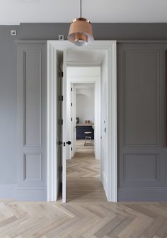 an open door leading into a room with gray walls and wood floors, along with a light fixture hanging from the ceiling