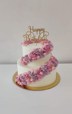 a three tiered cake with purple flowers on the bottom and gold lettering happy birthday