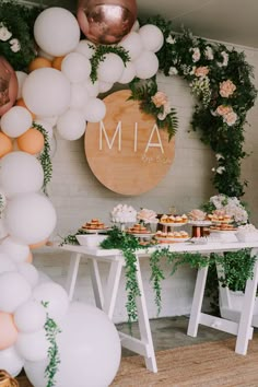 a table topped with lots of white balloons and greenery next to a sign that says mia