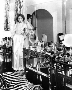 two women standing in front of a table full of pots and pans, with one woman looking at the mirror