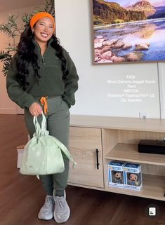 a woman standing in front of a tv holding a green bag and smiling at the camera