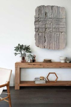 a wooden table sitting in front of a white wall with a painting on the wall