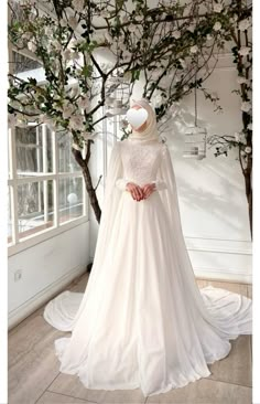 a woman in a white wedding dress standing next to a tree with flowers on it