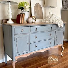 a blue dresser with two lamps and pictures on top