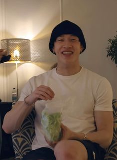 a man sitting in a chair holding a bunch of lettuce and smiling at the camera