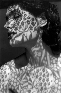 black and white photograph of a woman with her face painted in floral designs on her body