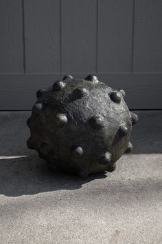 a large black ball sitting on top of cement next to a garage door, with rivets all over it