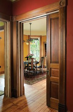 an open door leading to a dining room with red walls and wood floors, along with a chandelier hanging from the ceiling