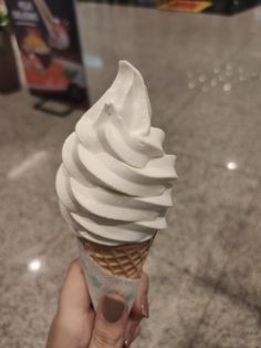 a hand holding an ice cream cone with white icing