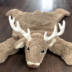 a stuffed moose head laying on top of a wooden floor next to a rug with antlers