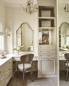 a white bathroom with two chairs and a chandelier above the sink, in front of a large mirror