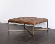 a brown ottoman sitting on top of a hard wood floor next to a white wall